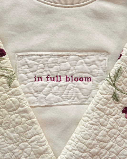 Close-up of a quilted fabric with embroidered text 'in full bloom'