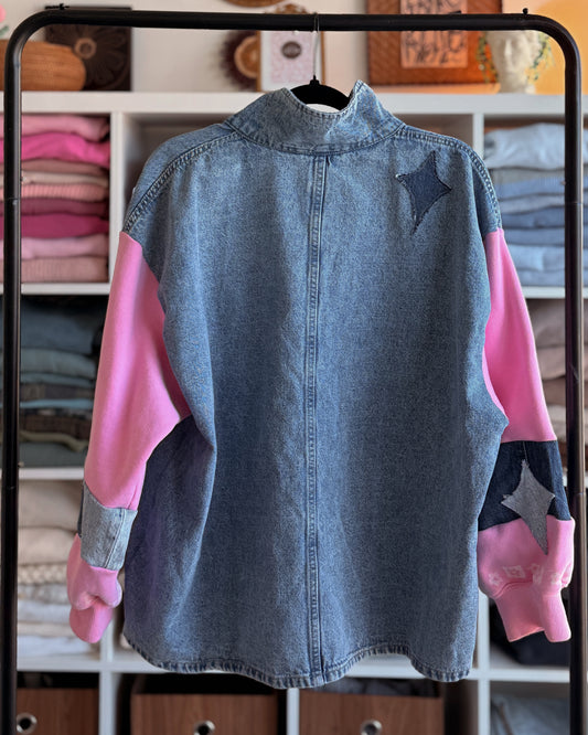 Denim shirt with pink sleeves on a hanger against a background of folded clothes.