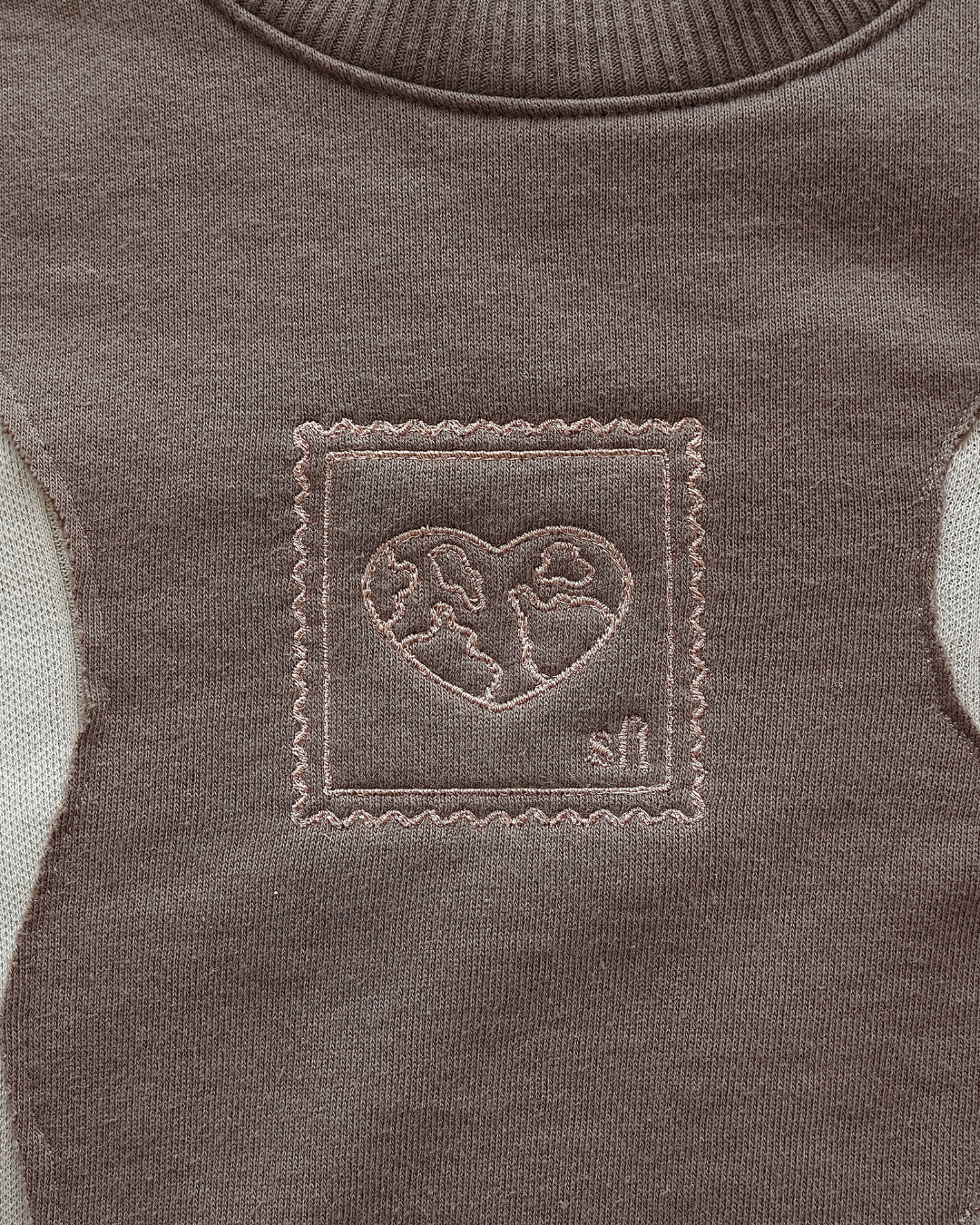 Close-up of a brown sweater with a heart-shaped earth and sft logo