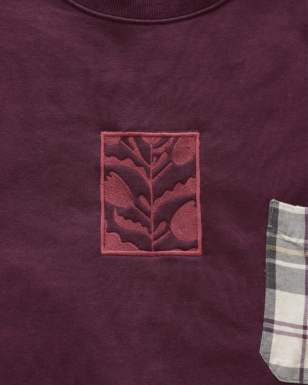 Maroon sweatshirt with a leaf emblem and plaid pocket