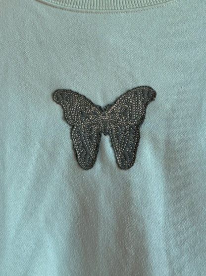 Butterfly patch on a light green crewneck close up